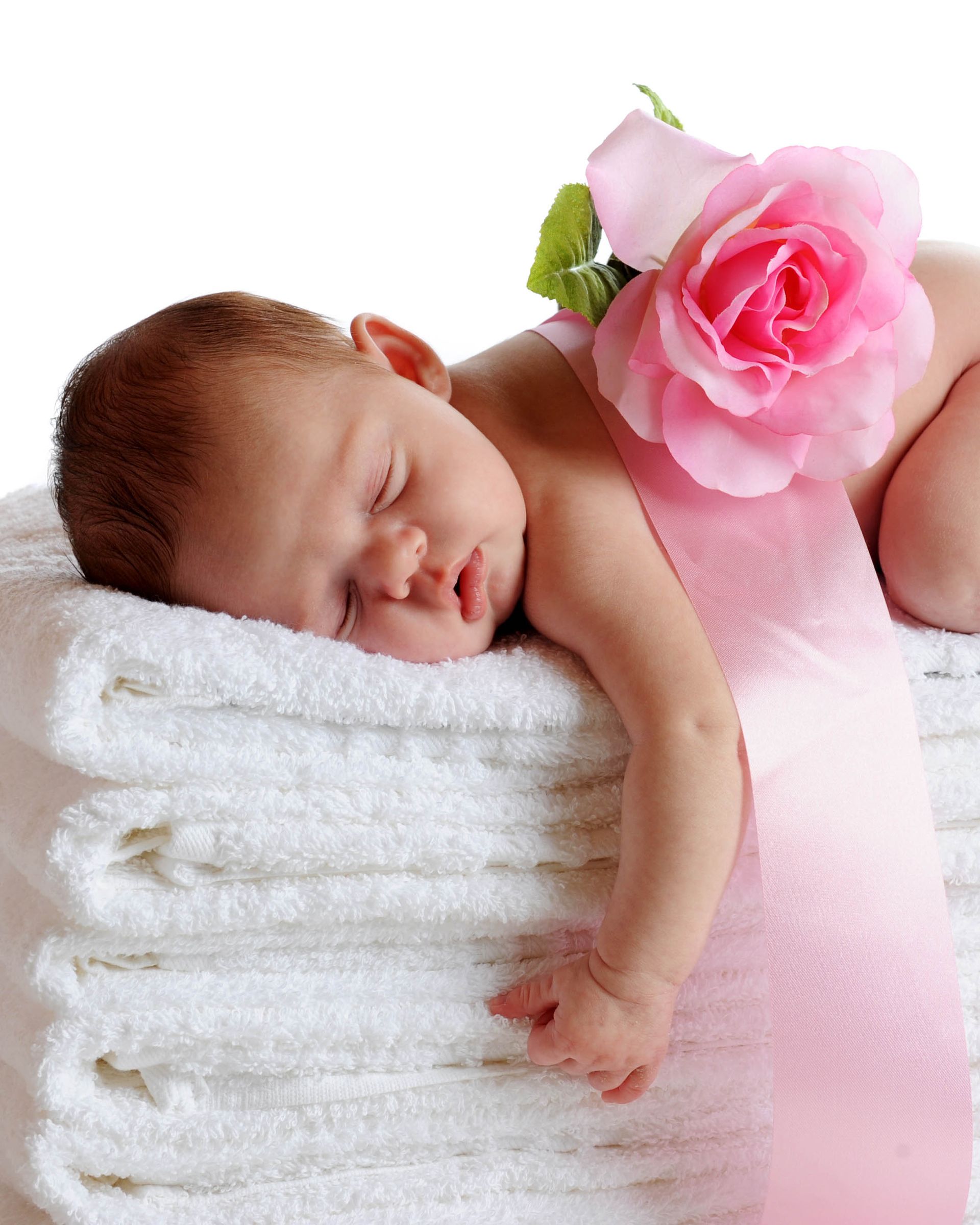 Baby sleeping on a stack of white towels, pink rose and ribbon.