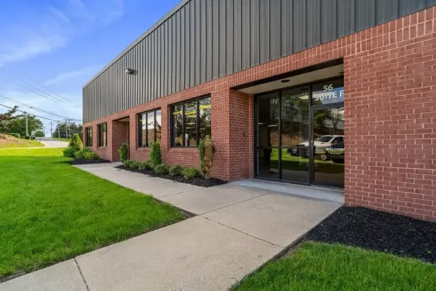 Brick office building with large glass windows, concrete walkway, and green lawn on a sunny day