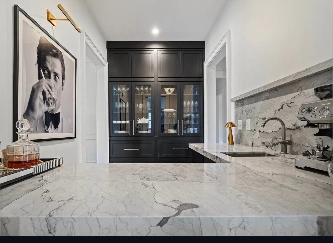 Bright modern kitchen with marble island, black cabinets, brass fixtures, and a framed portrait on the wall