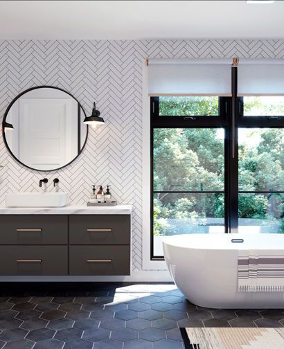Modern bathroom with dark vanity, round mirror, black hex tile, and freestanding tub by a large window