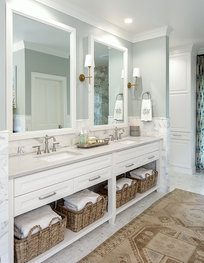 Bright white bathroom vanity with two mirrors, woven baskets, and a beige patterned rug