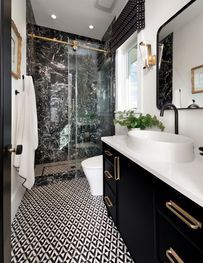 Modern black-and-white bathroom with patterned floor, walk-in glass shower, and white vanity sink