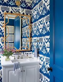 Blue-and-white patterned bathroom with a white vanity, gold-framed mirror, and blue door
