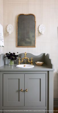 Gray bathroom vanity with gold faucet, scalloped mirror, and white wall sconces