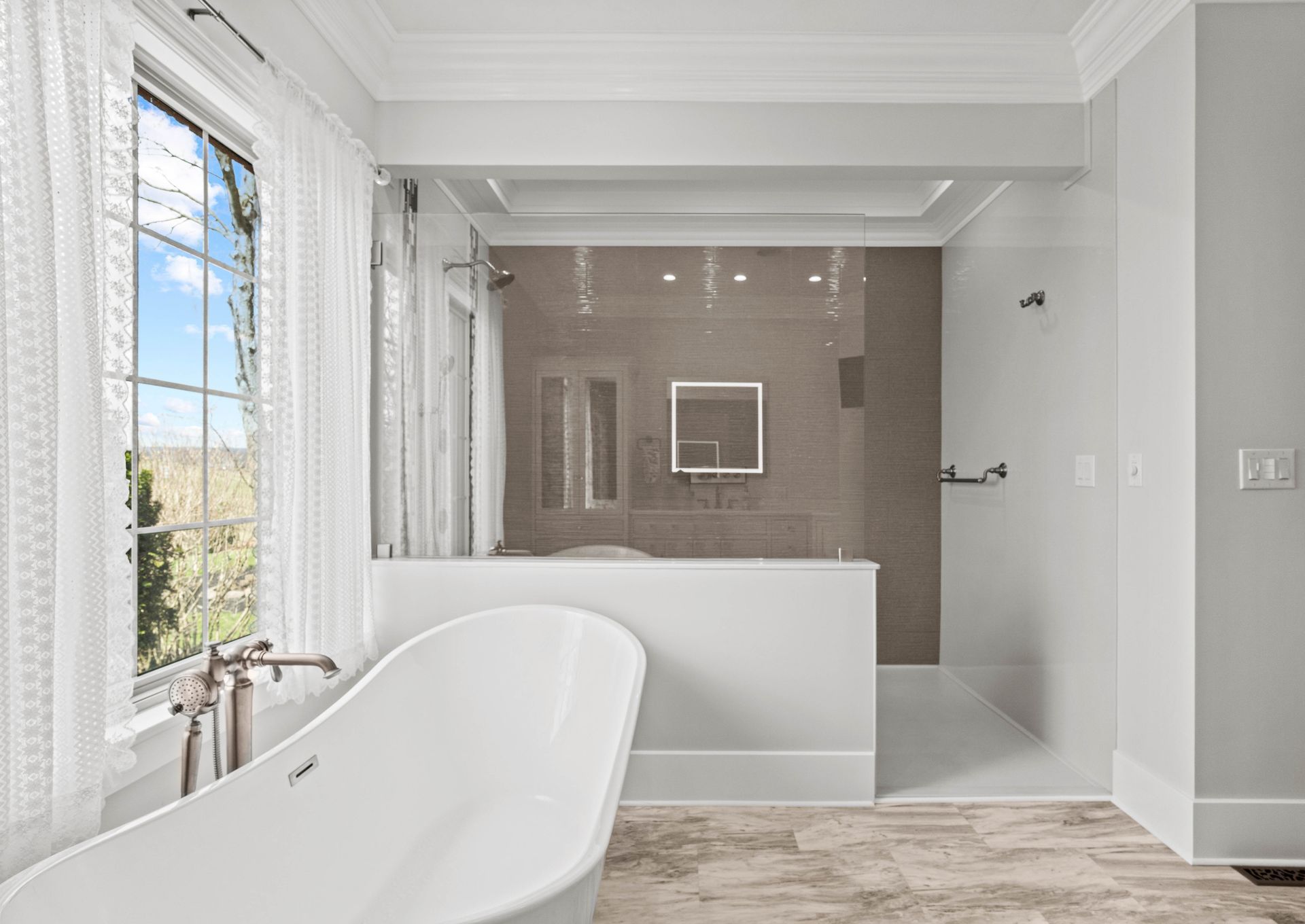 Bright modern bathroom with freestanding tub, glass shower, and large window