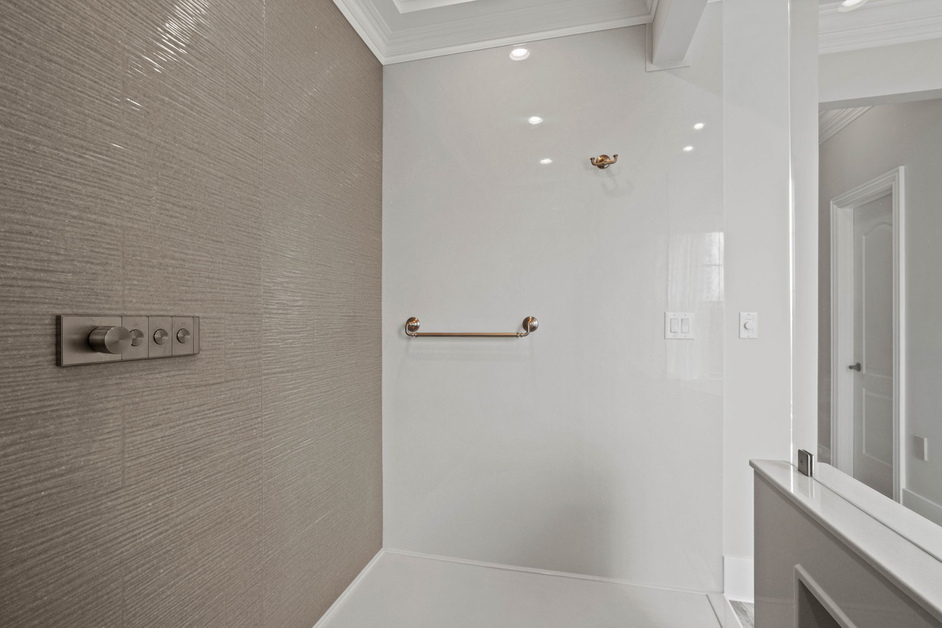 Modern bathroom with walk-in shower, grab bar, white walls, and textured gray tile