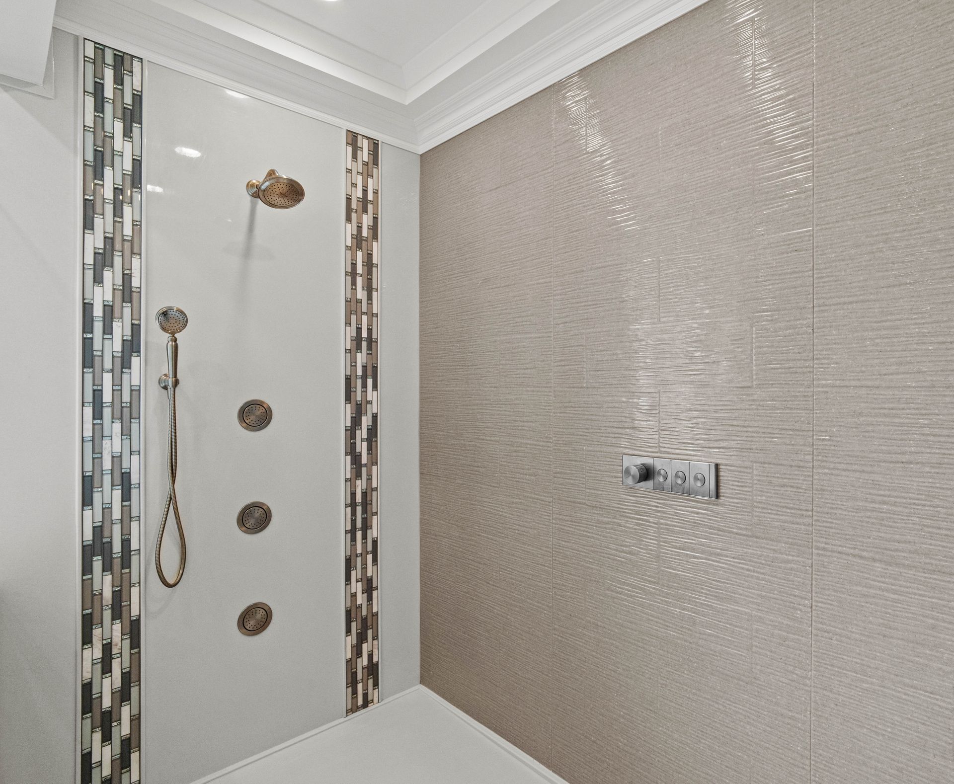 Modern tiled shower with rainfall head, handheld sprayer, and wall controls.