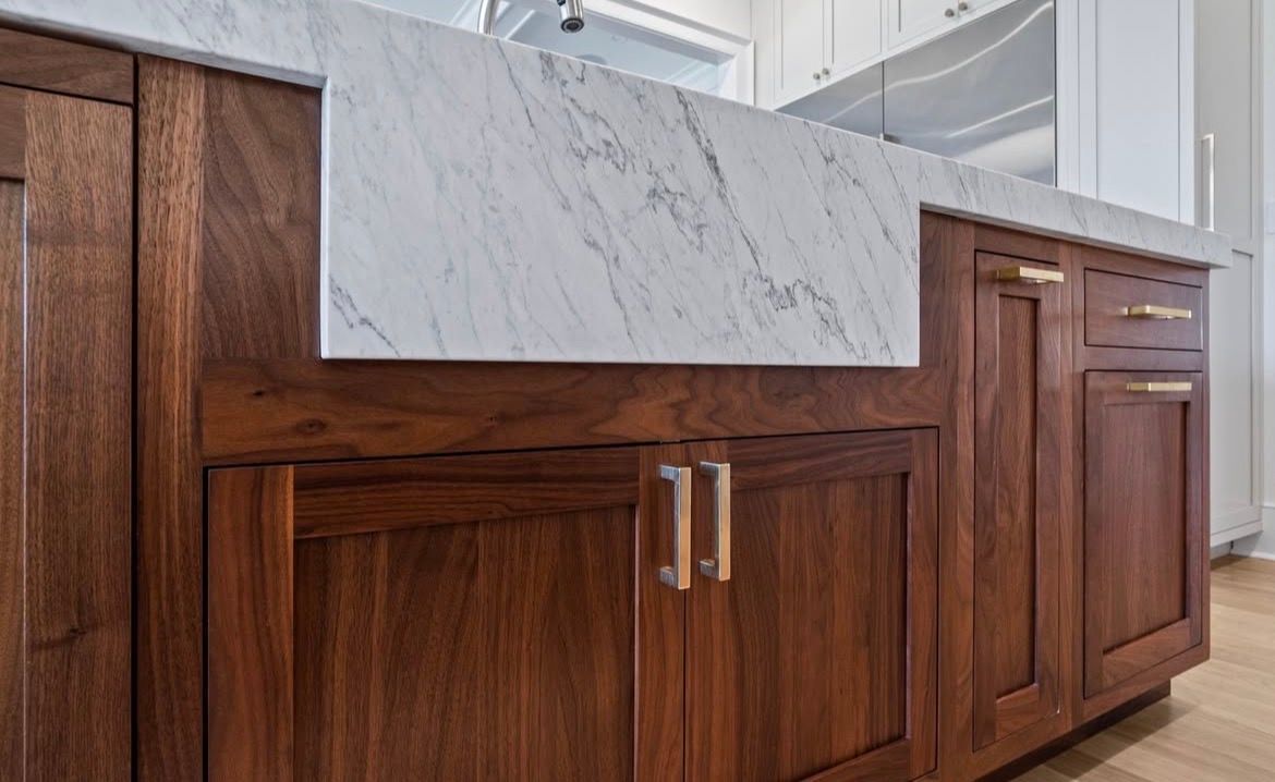 Wooden bathroom vanity with a gray marble countertop and double sinks under a bright mirror.