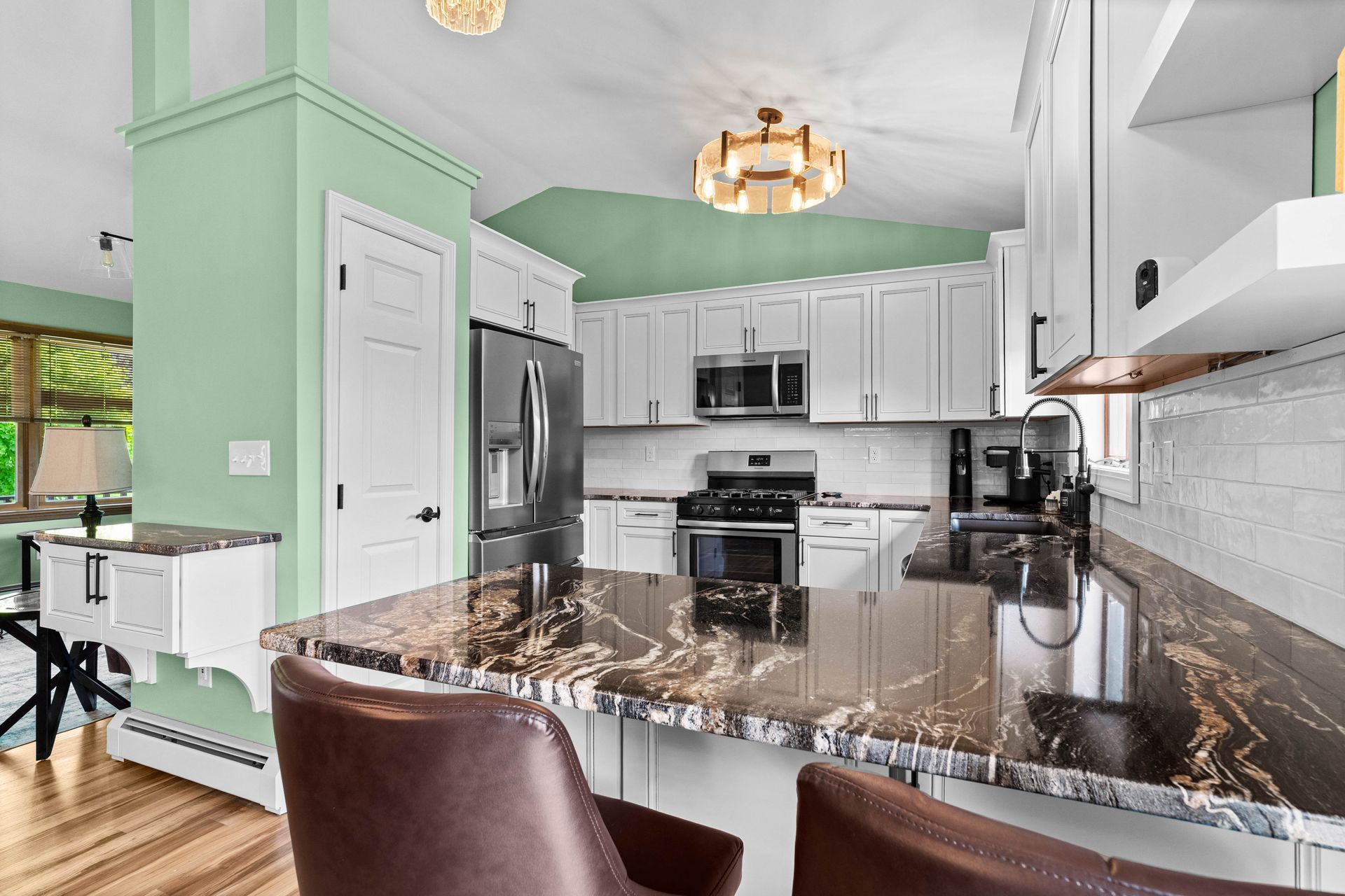 Bright white kitchen with marble island, stainless appliances, mint green walls, and brown barstools