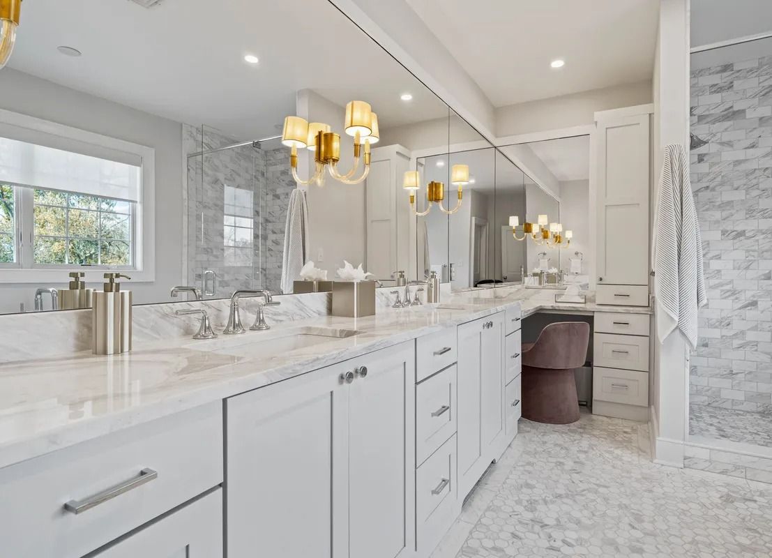 Bright modern bathroom with double vanity, marble countertops, gold fixtures, and large mirrors