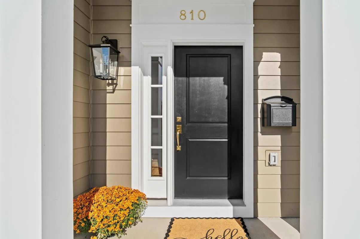 Front entryway with black door, white trim, wall lantern, mailbox, and orange flowers by the step.
