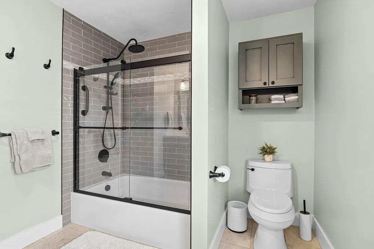 Modern bathroom with glass shower, gray tile, white toilet, and wall cabinet over a small plant.