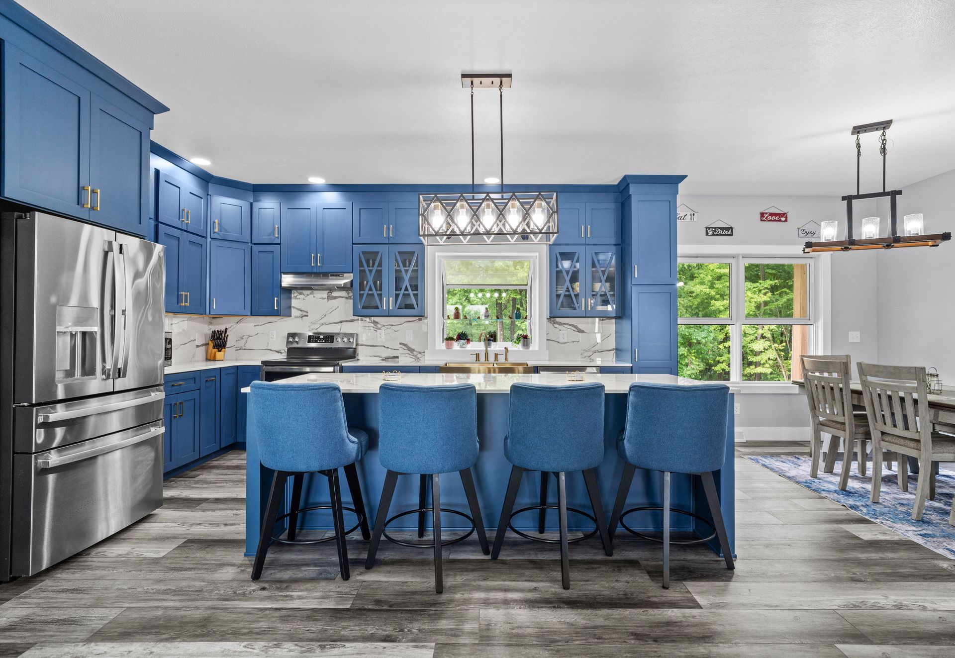 Blue kitchen with island, barstools, stainless fridge, and dining area with large windows