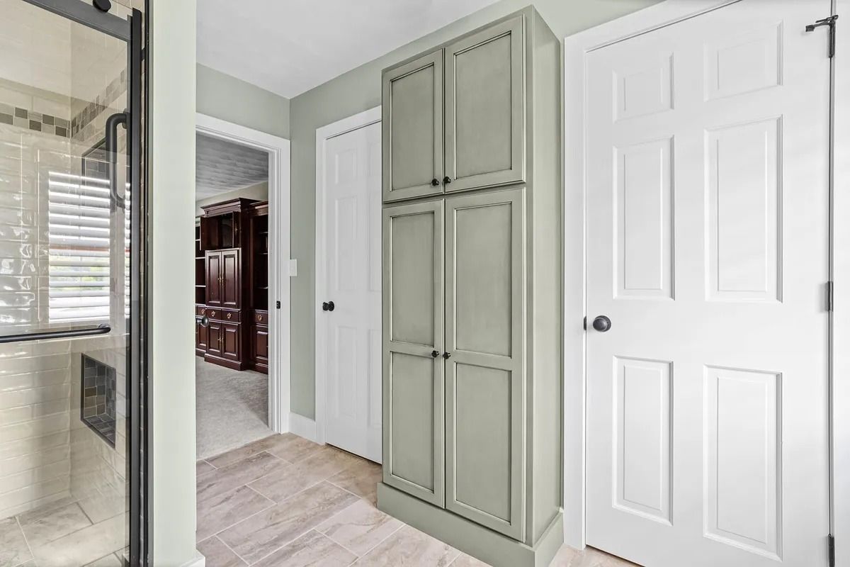 Bathroom with glass shower, pale green cabinets, and white doors in a bright interior