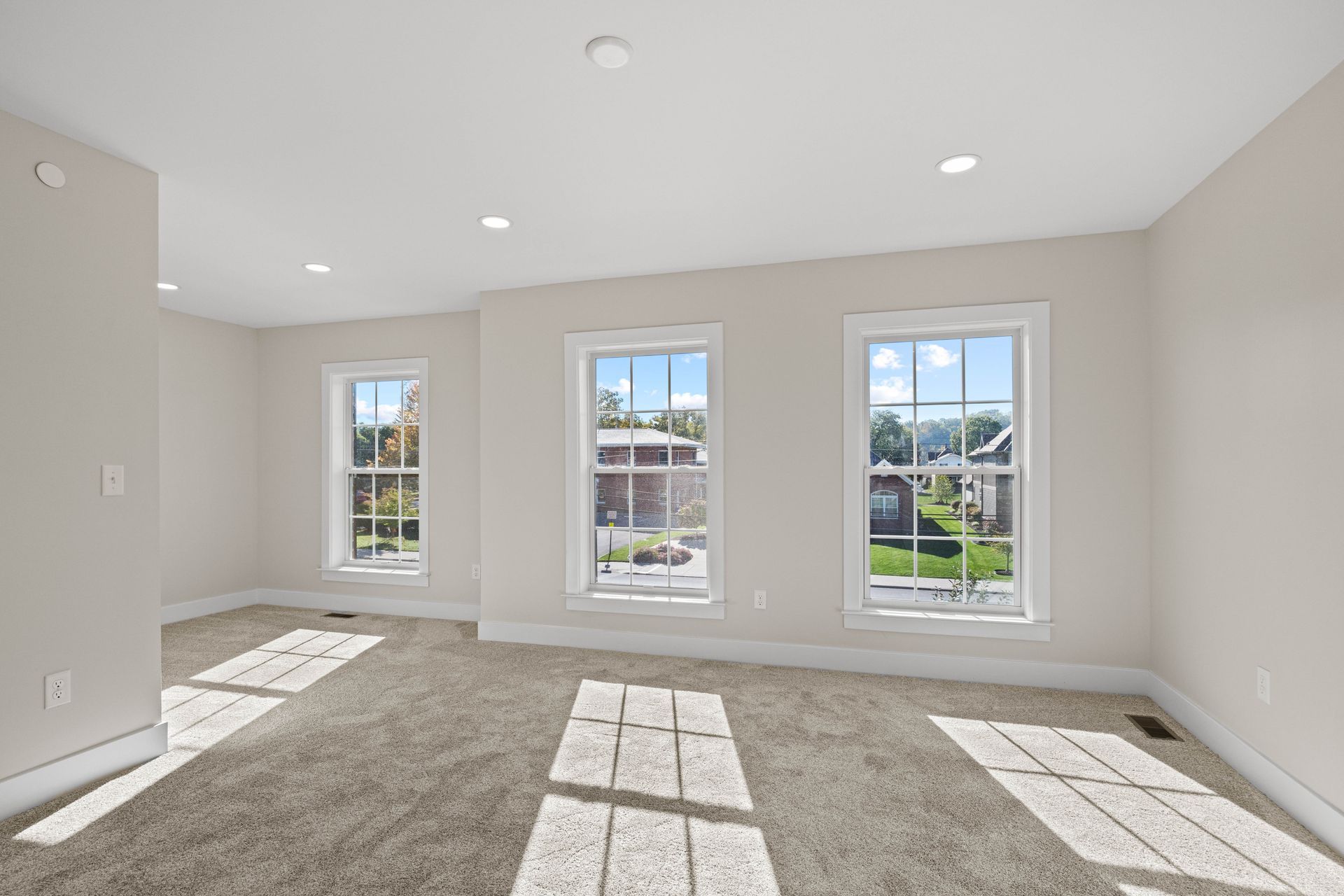 Bright empty room with beige carpet, white walls, and three tall windows letting in sunlight.