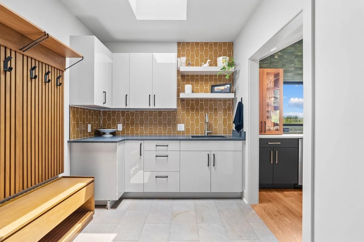 Modern kitchen with white cabinets, wood backsplash, and a bench by the entryway