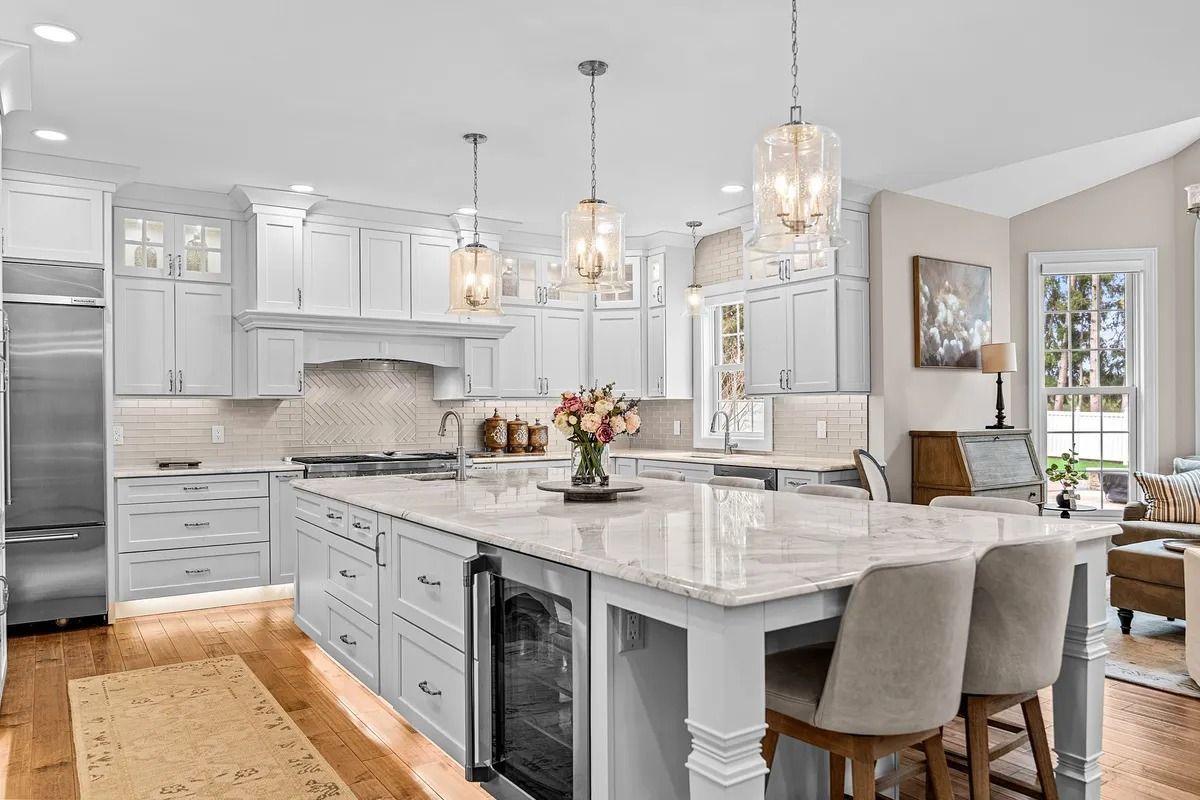 Bright modern kitchen with white cabinets, marble island, pendant lights, and upholstered barstools
