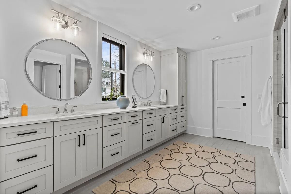 Bright modern bathroom with double vanity, round mirrors, white cabinets, and patterned floor tile.