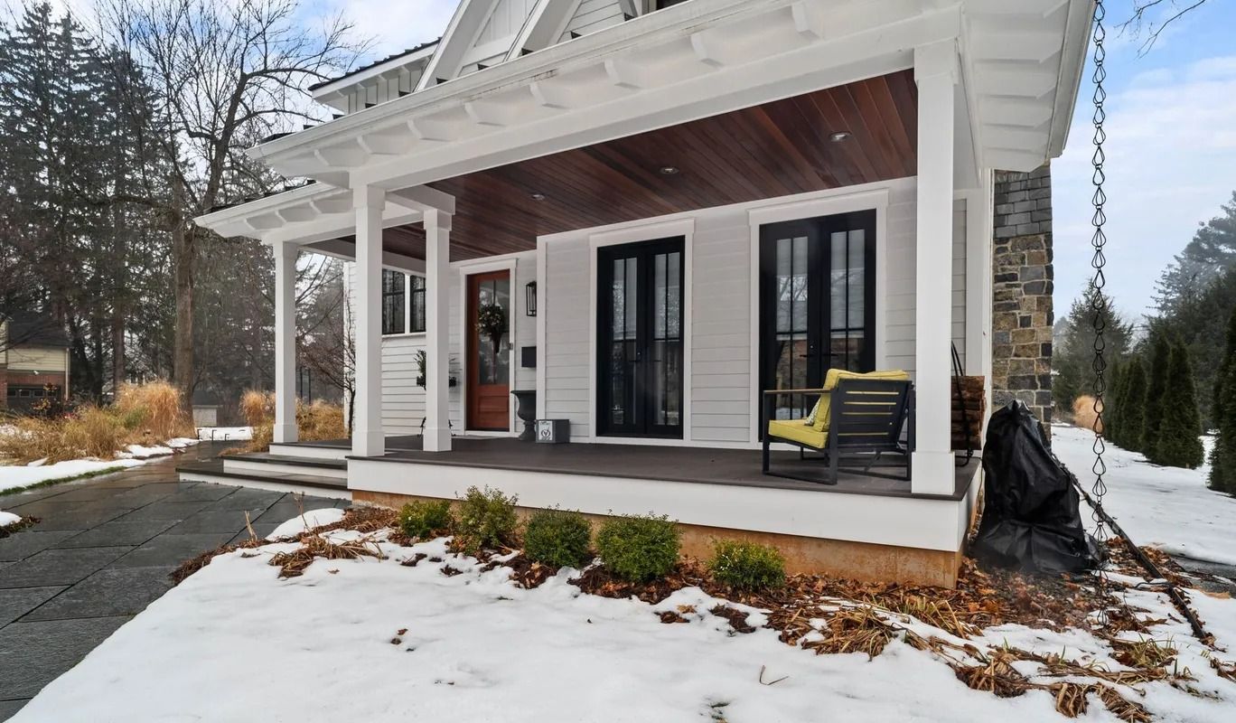 Snowy front porch of a white house with black shutters and a covered sitting area
