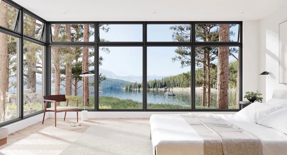 Modern bedroom with floor-to-ceiling windows overlooking a lake and trees, white bed and chair.