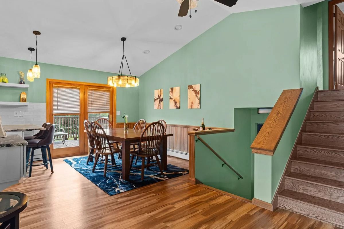 Dining room with green walls, wooden table, blue rug, and staircase railing