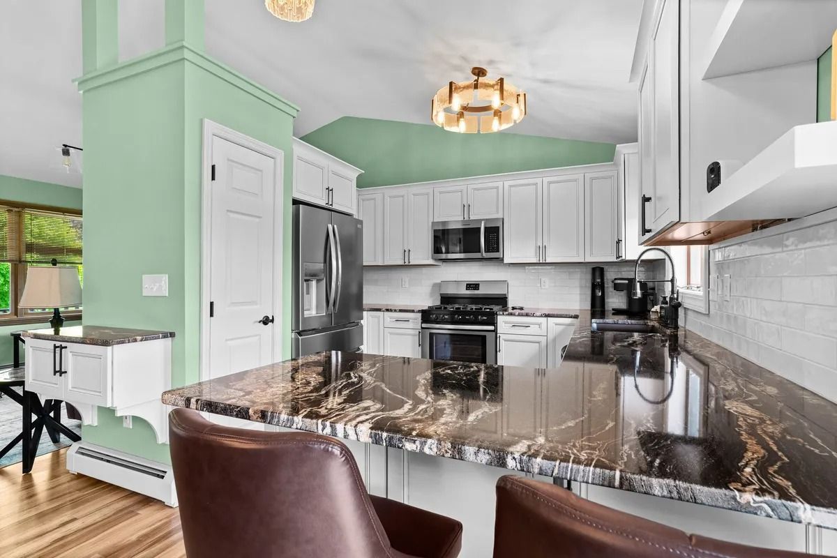 Bright white kitchen with green walls, dark granite island, stainless appliances, and two brown bar stools