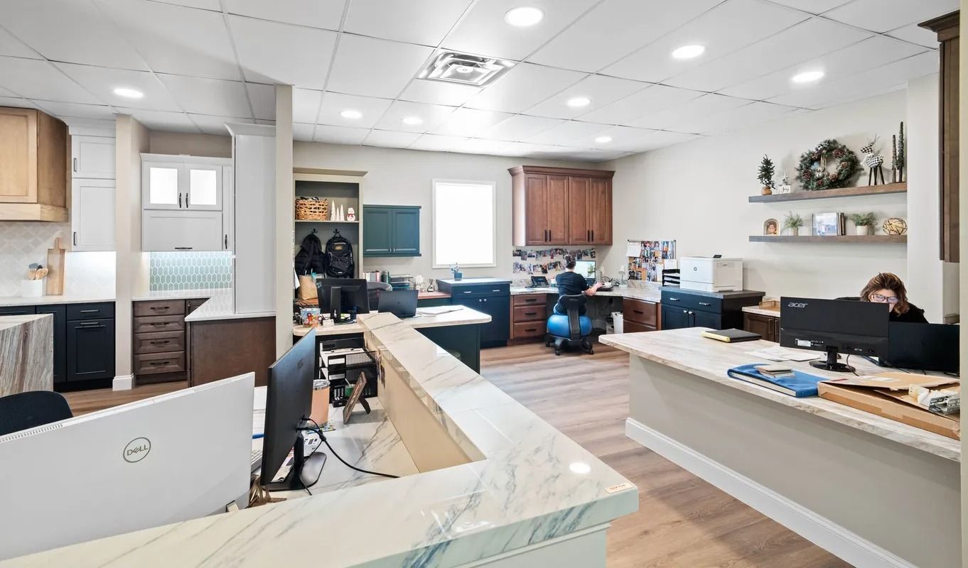 Bright open office lounge with desks, computers, sofas, and two people working or sitting in a modern space