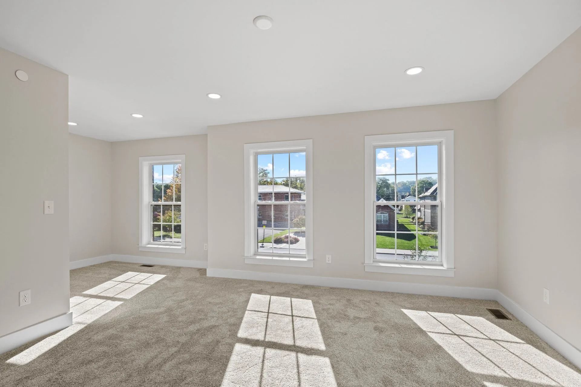 Bright empty room with beige carpet, white walls, and three tall windows letting in sunlight.
