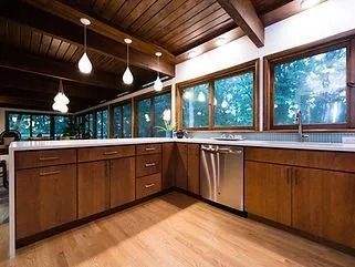 Modern kitchen with wood cabinets, white countertops, pendant lights, and large windows overlooking trees