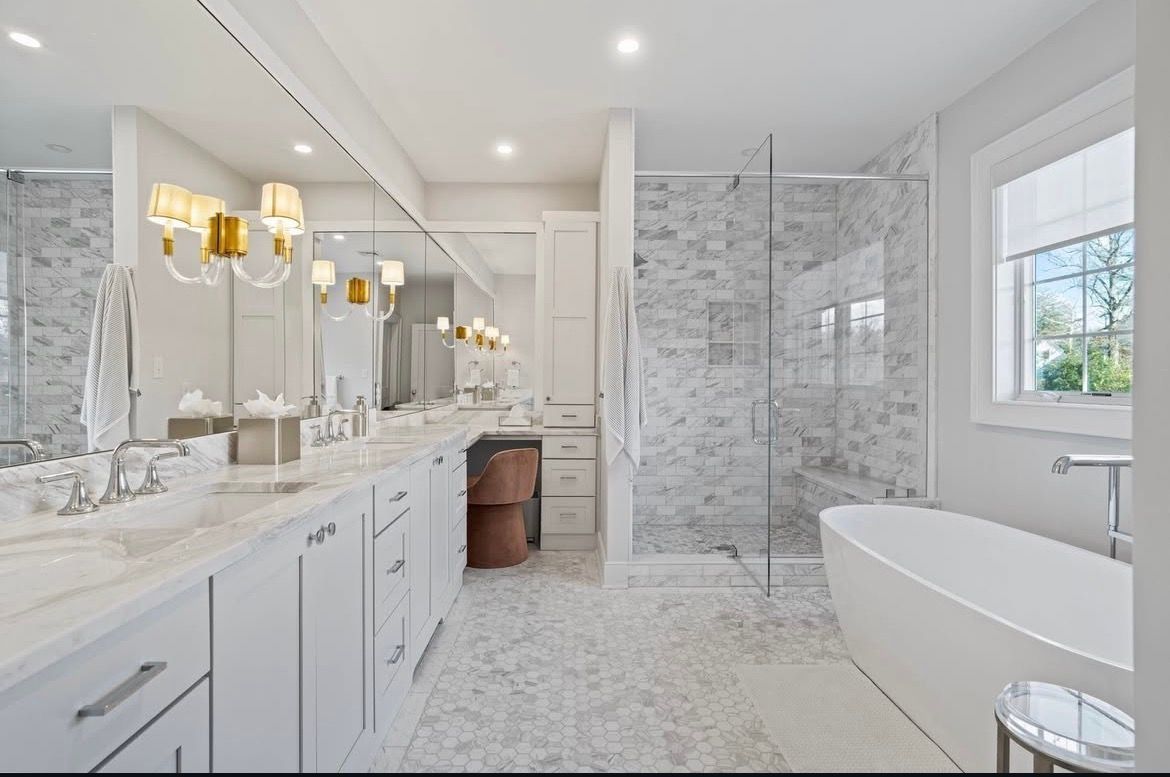 Bright marble tiles with double vanity, glass shower, and freestanding tub by a window.