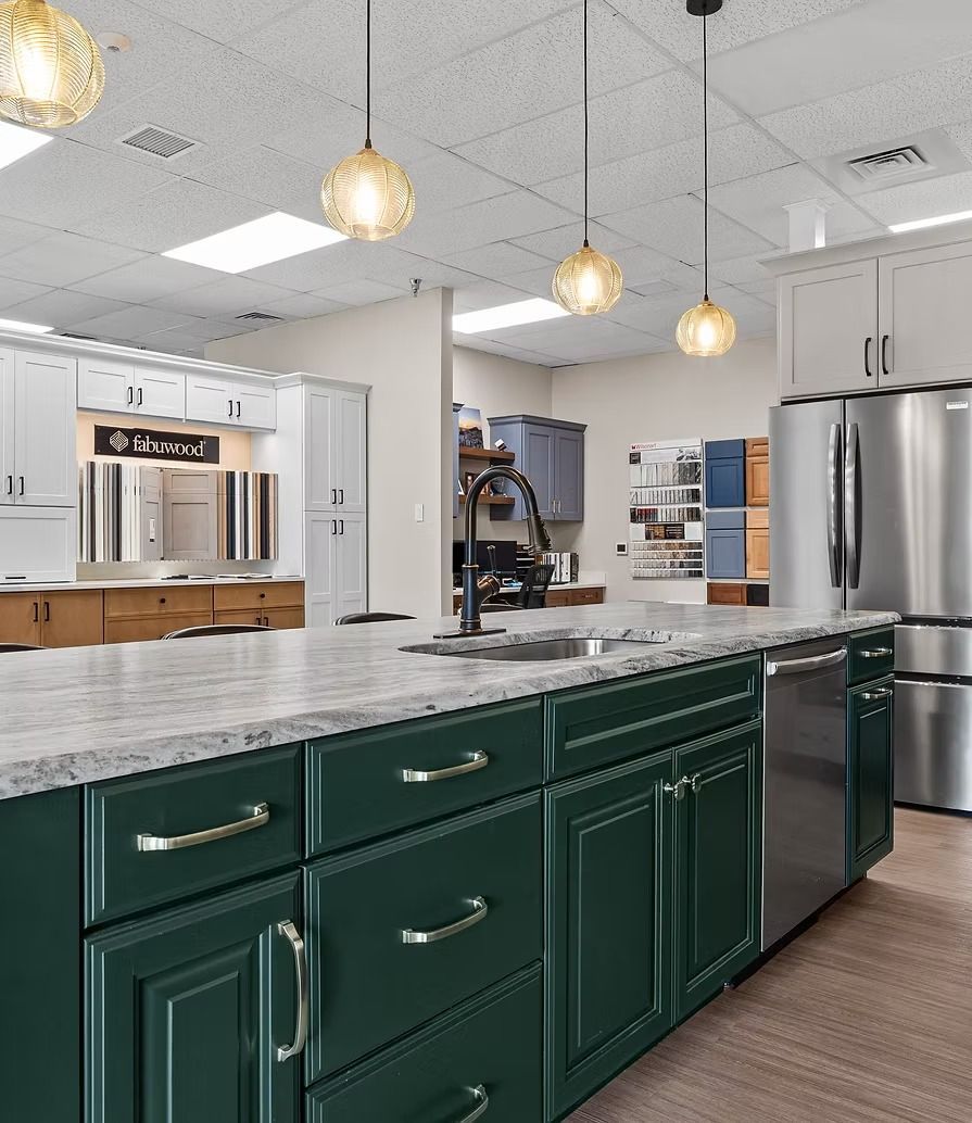 Modern kitchen showroom with green cabinets, marble island, pendant lights, and stainless steel appliances