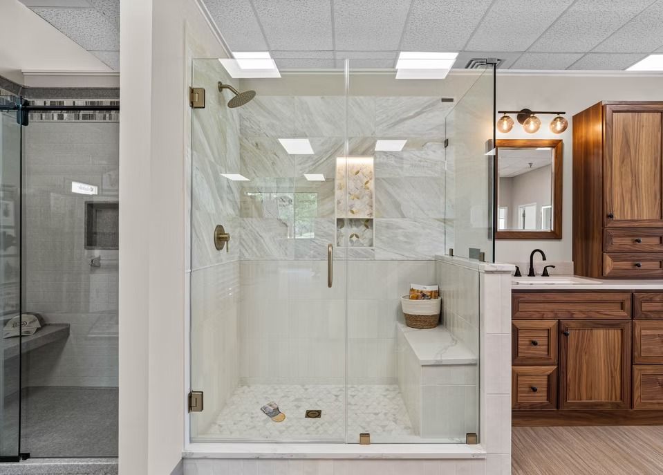 Modern walk-in shower with white marble tile, glass enclosure, and adjacent wooden vanity in a bright bathroom