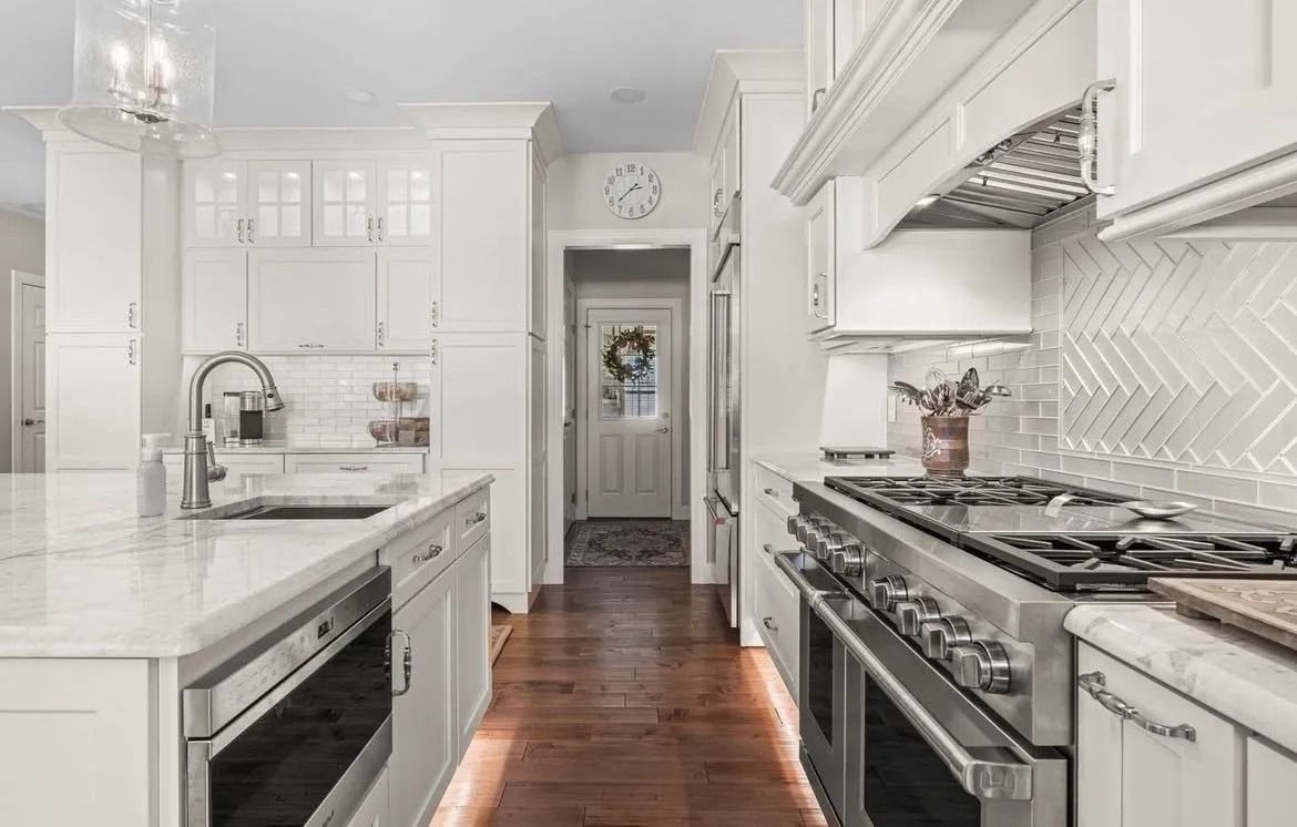 Bright white modern kitchen with stainless steel appliances and dark wood floor, viewed down a narrow aisle