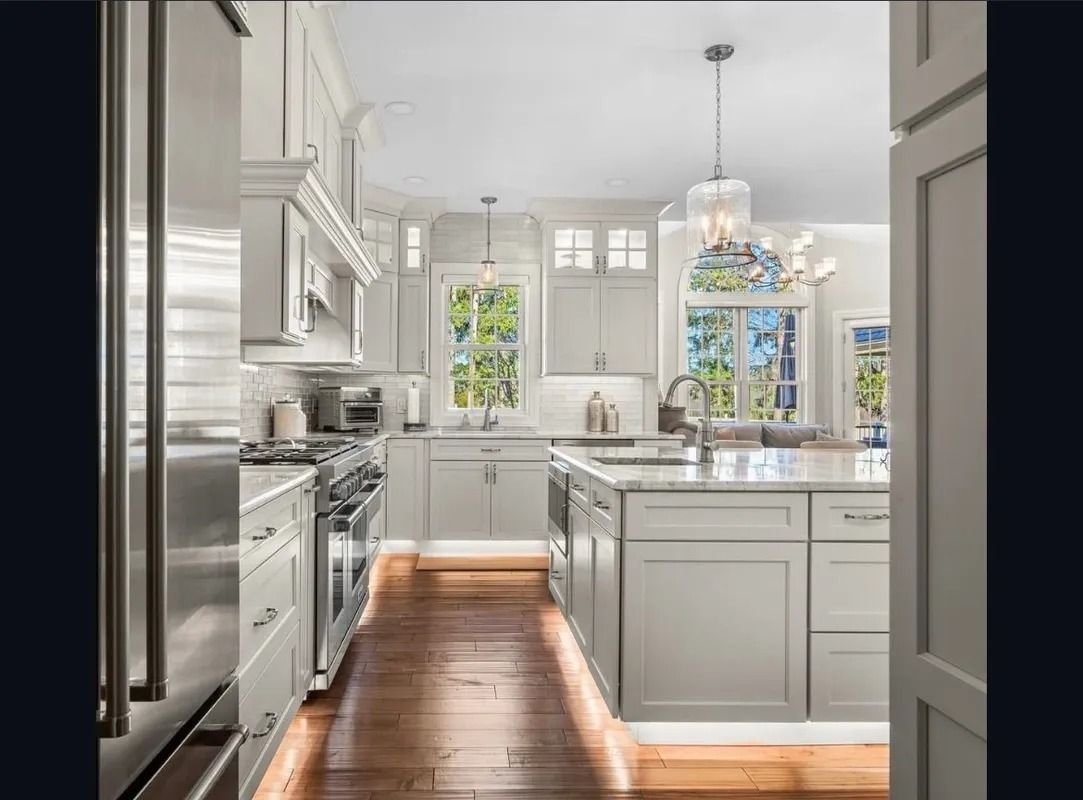 Bright white kitchen with island, stainless appliances, hardwood floors, and hanging pendant lights