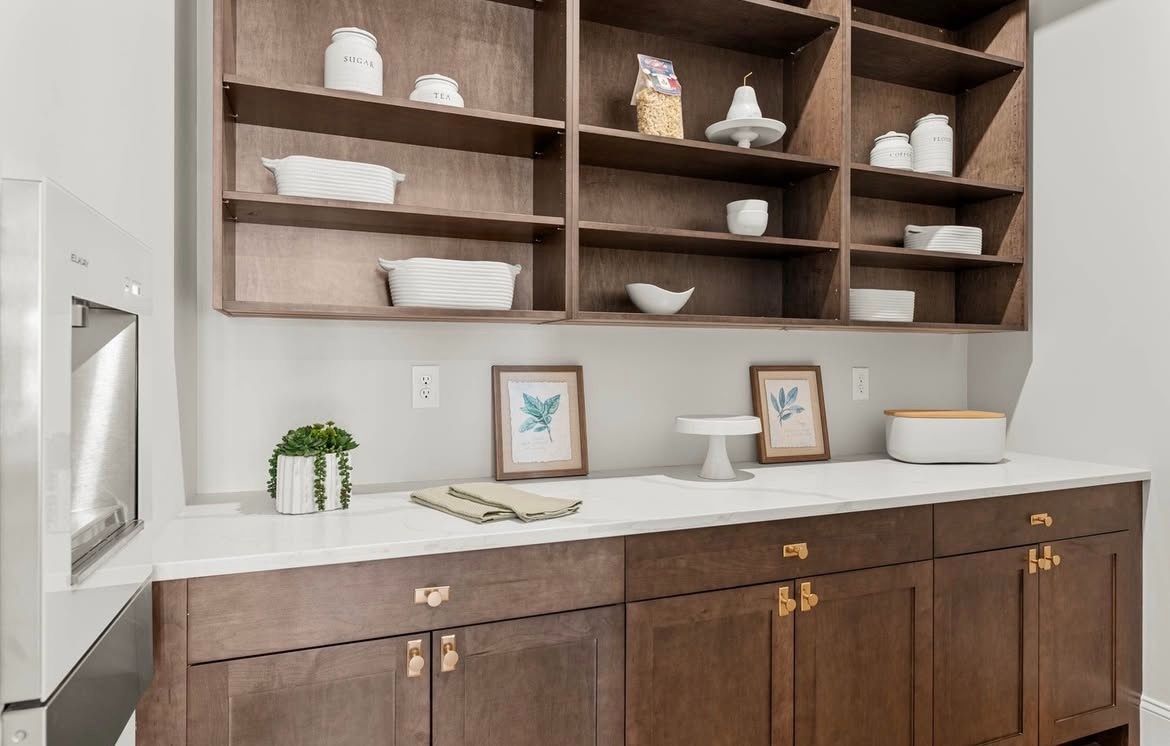 Kitchen buffet with dark wood cabinets, white countertop, and open shelves with decor and dishes