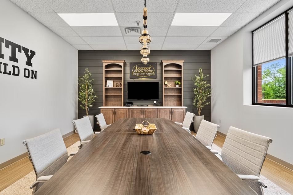 Modern conference room with long wooden table, white chairs, wall shelves, and a TV at the far end