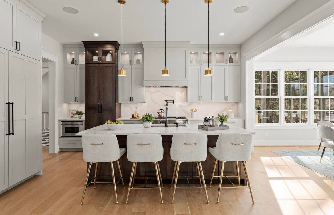 Bright white kitchen with island, bar stools, stainless fridge, and large windows letting in sunlight