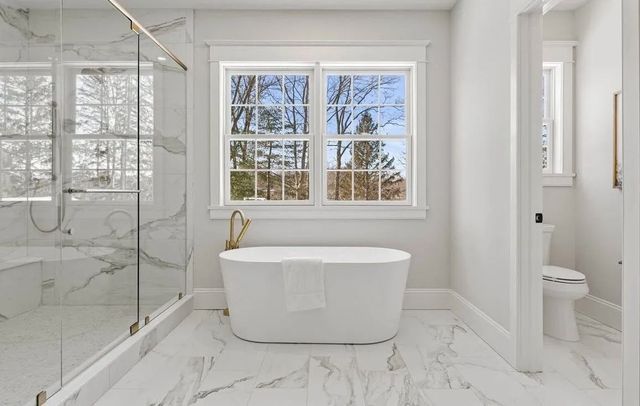 Bright modern bathroom with freestanding tub, glass shower, marble floors, and snowy window view.