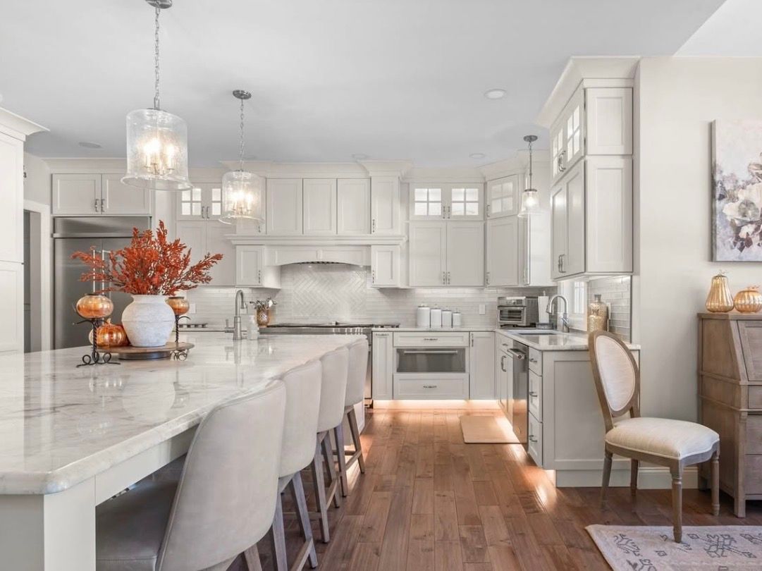 Bright white kitchen with marble island, pendant lights, and a wooden floor with autumn decor.