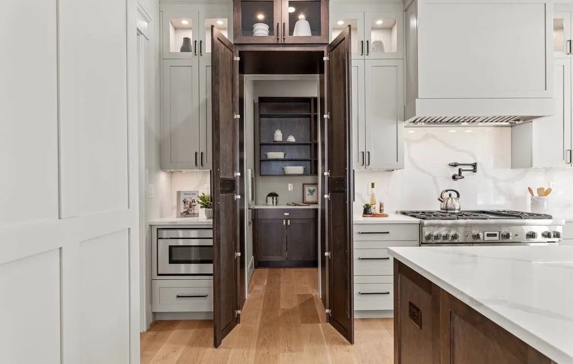 Modern white kitchen with open pantry doors, wood floor, and marble island countertop