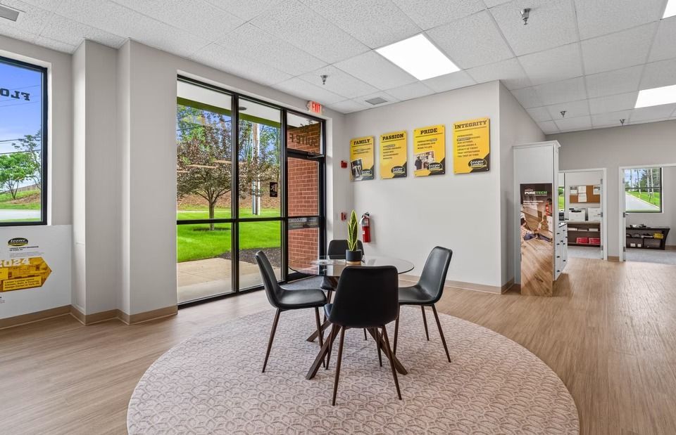 Bright modern office waiting area with black chairs, round table, large windows, and yellow wall art.