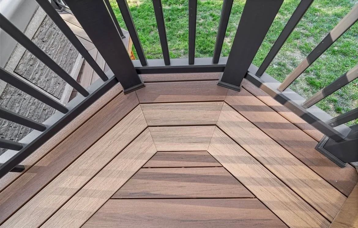 Wooden deck corner with black railings overlooking greenery and gravel below