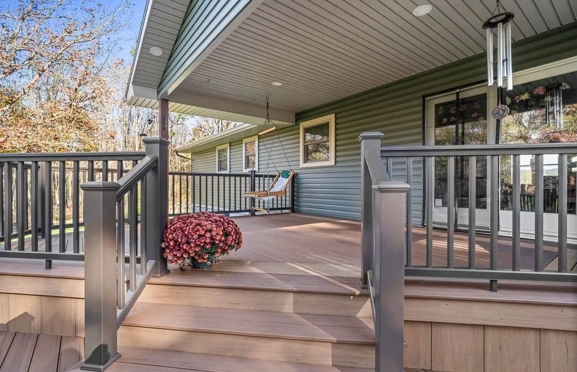 Covered front porch with wooden steps, gray railings, and a potted red flower under a green roof