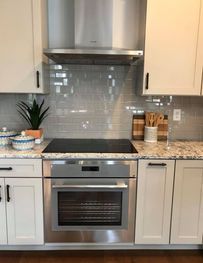 Modern kitchen with stainless steel oven, black cooktop, and light cabinets on granite countertops.