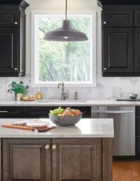 Modern kitchen with black cabinets, white island, large window, and bowl of fruit on the counter