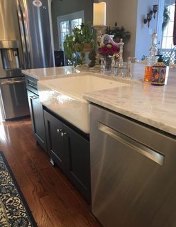 Modern kitchen island with white countertop, stainless steel dishwasher, dark cabinets, and hardwood floor