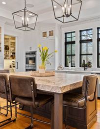 Modern kitchen with marble island, brown stools, pendant lights, and black-framed windows