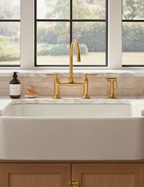 Modern kitchen sink with gold faucet beneath a window, white basin, and soap dispenser on the counter.