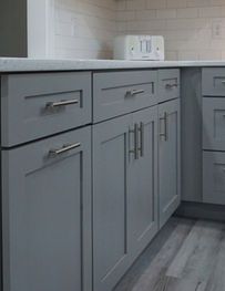 Gray kitchen cabinets with silver handles beneath a white countertop and tiled backsplash.
