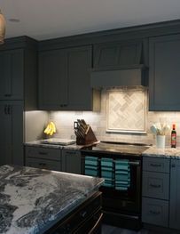 Dark teal kitchen with black stove, marble island, and light tile backsplash